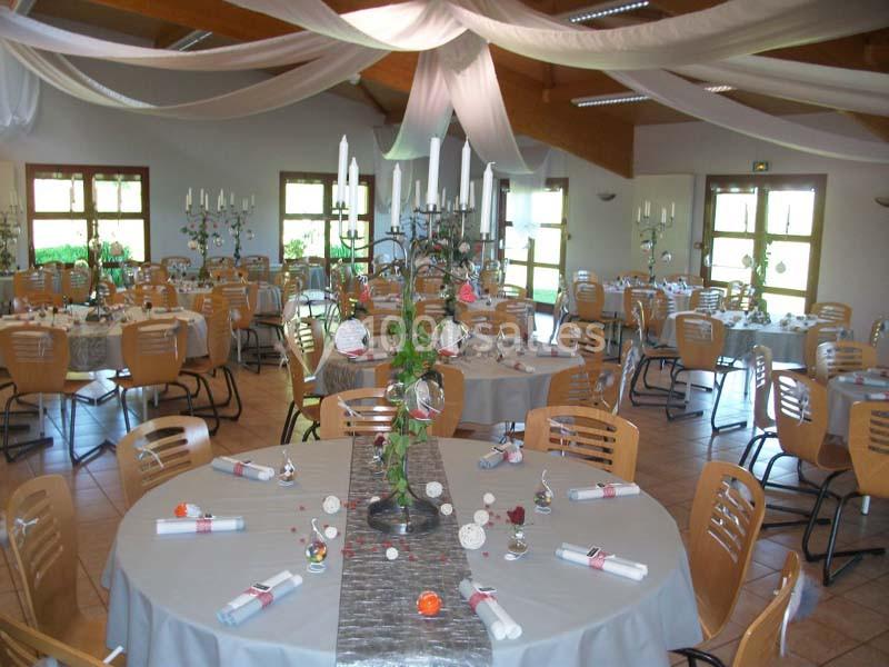 Salle de réception décorée pour un événement, avec tables rondes, nappes grises, bougies et chaises en bois.
