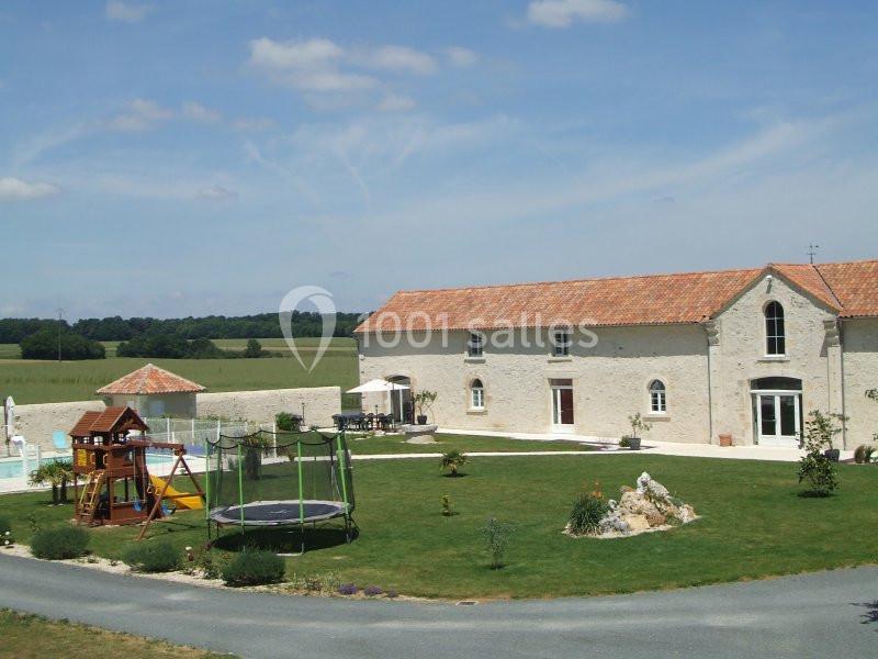Grande maison en pierre avec jardin, trampoline, aire de jeux et piscine, située dans un cadre rural.
