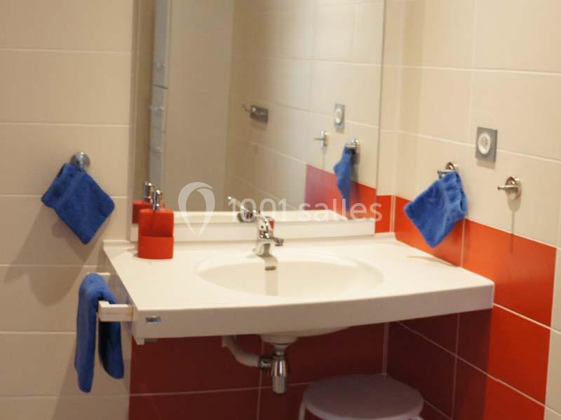 Lavabo blanc avec miroir, serviettes bleues accrochées et carrelage mural rouge et blanc dans une salle de bain.