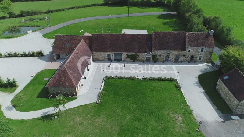 Vue aérienne d'un bâtiment en pierre avec toits en tuiles, entouré de pelouses et d'allées gravillonnées.