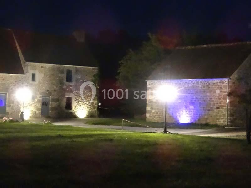 Deux bâtiments en pierre éclairés par des lampadaires, entourés de pelouse, dans un cadre nocturne.