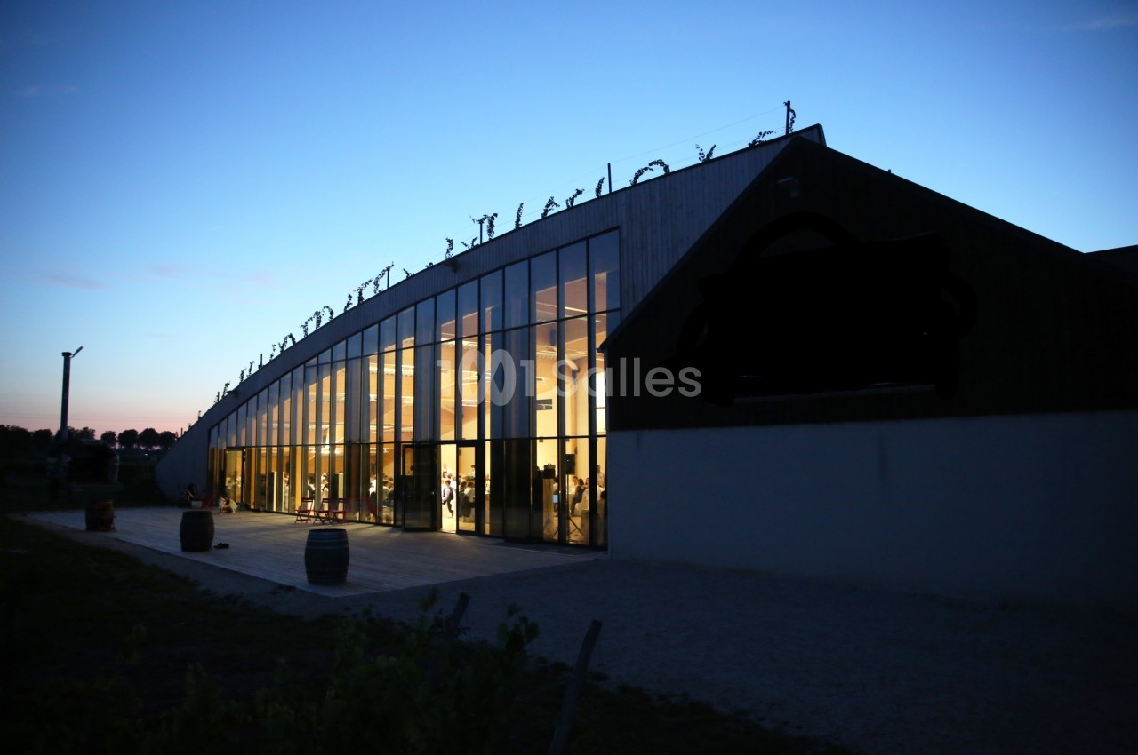 Bâtiment moderne avec de grandes baies vitrées illuminées, photographié au crépuscule.