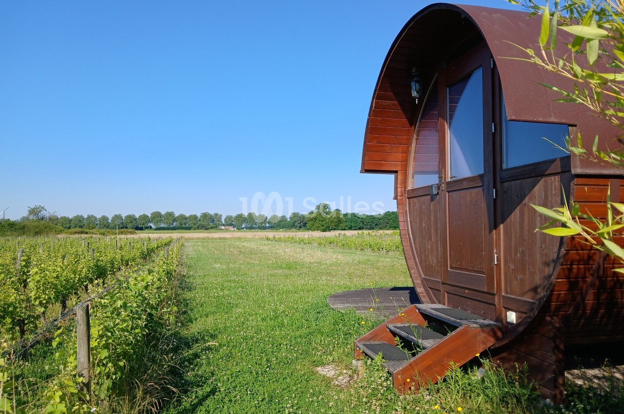 Cabane en bois arrondie dans un champ verdoyant sous un ciel bleu clair.