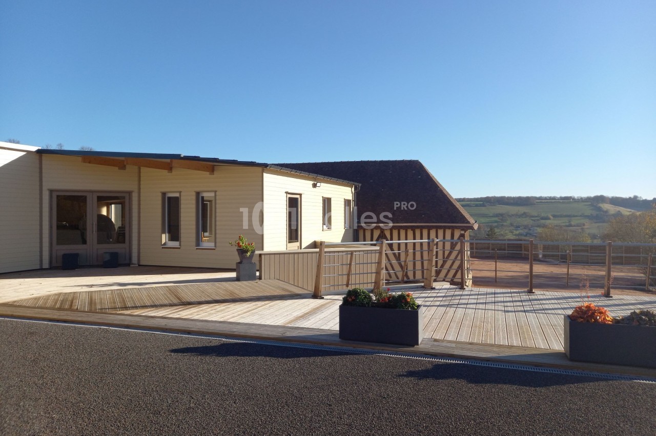 Bâtiment moderne en bois avec terrasse, situé dans un environnement rural sous un ciel dégagé.