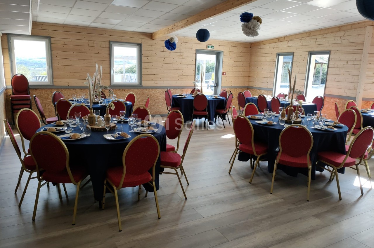 Salle décorée avec des tables rondes dressées, chaises rouges et fenêtres laissant entrer la lumière naturelle.