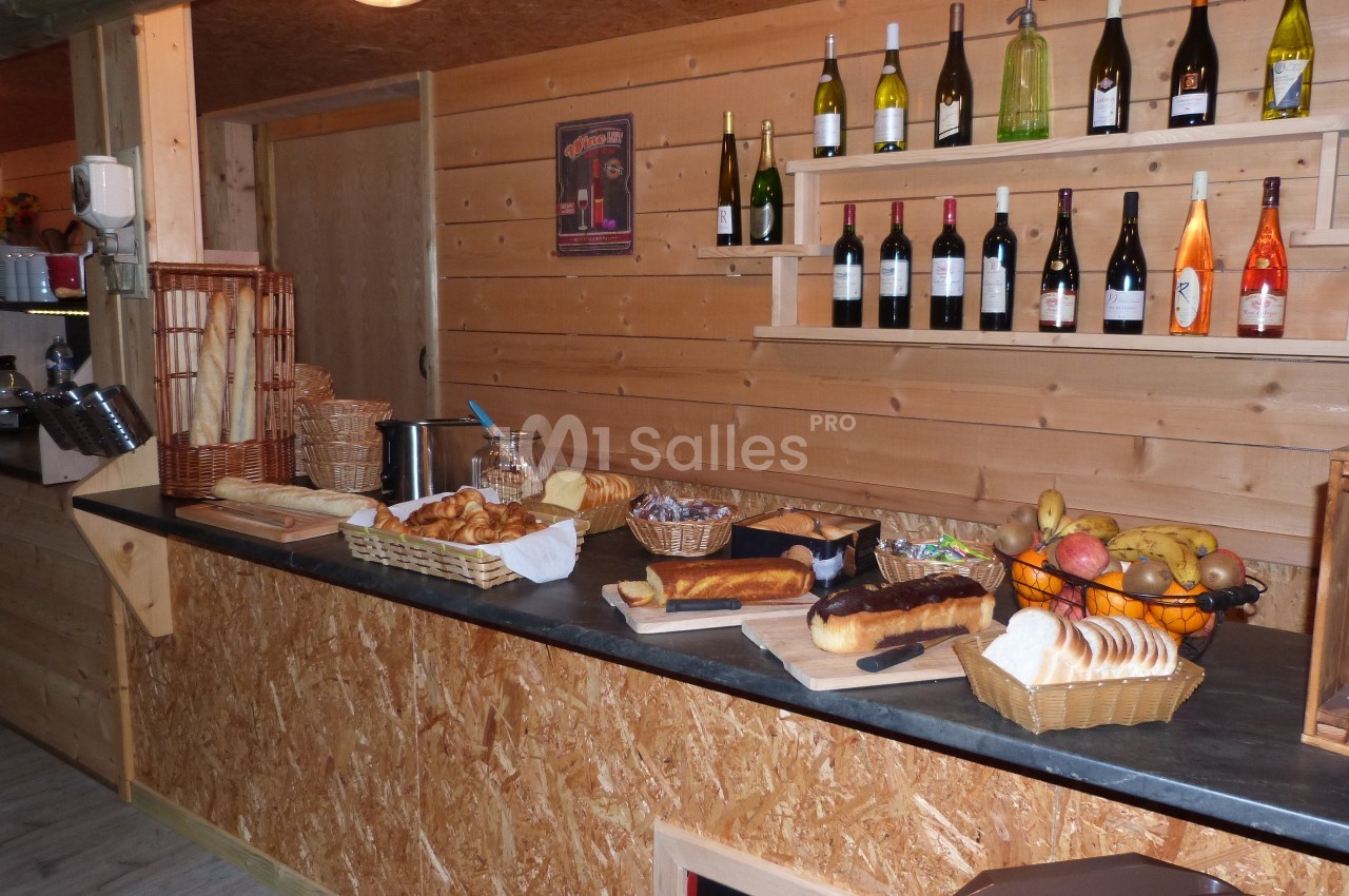 Buffet en bois avec pains, viennoiseries, fruits et bouteilles de vin alignées sur des étagères murales.