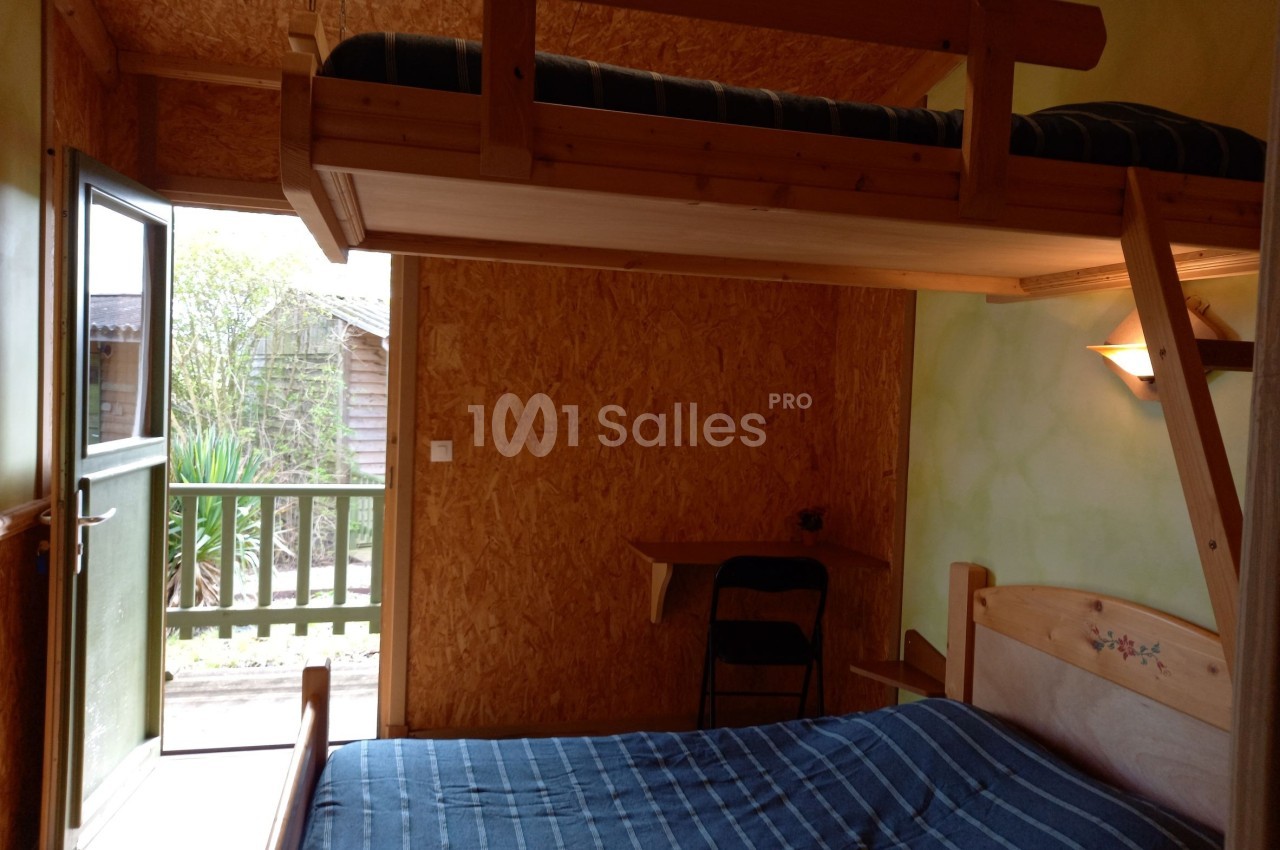 Chambre en bois avec lit superposé, lit double, bureau, chaise et porte ouverte donnant sur un extérieur verdoyant.