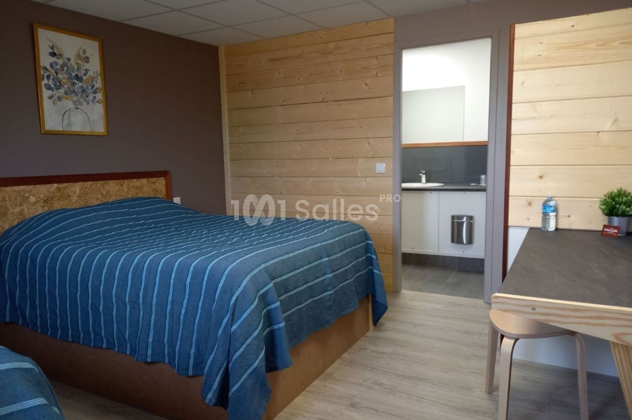 Chambre avec lit double, murs en bois, bureau, et vue sur une salle de bain moderne avec lavabo.