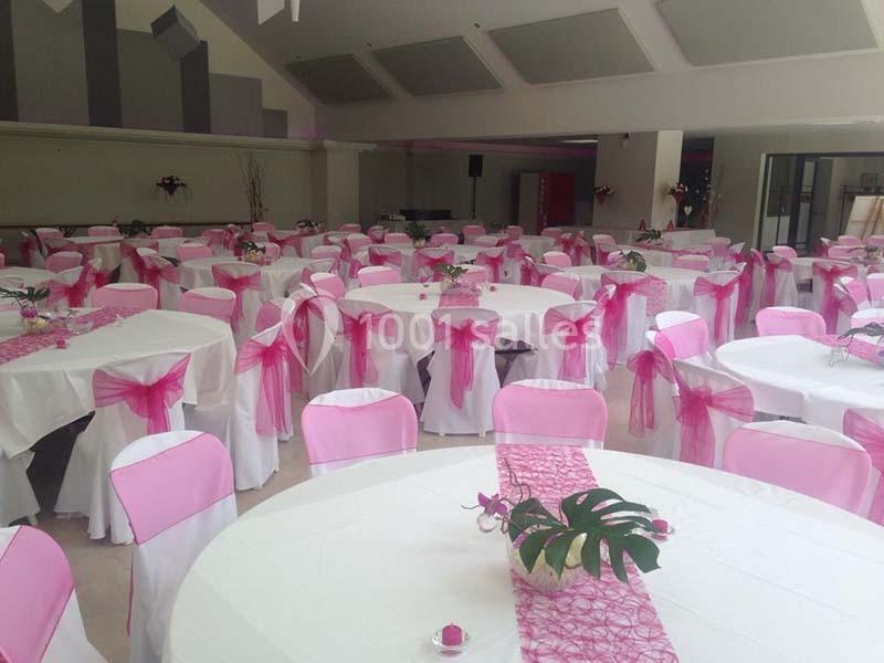 Salle de réception décorée avec des nappes blanches et des chaises ornées de nœuds roses.