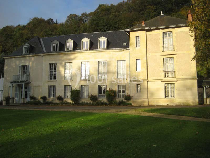 Façade d'un grand bâtiment ancien en pierre, entouré de pelouse et d'arbres, sous une lumière douce.
