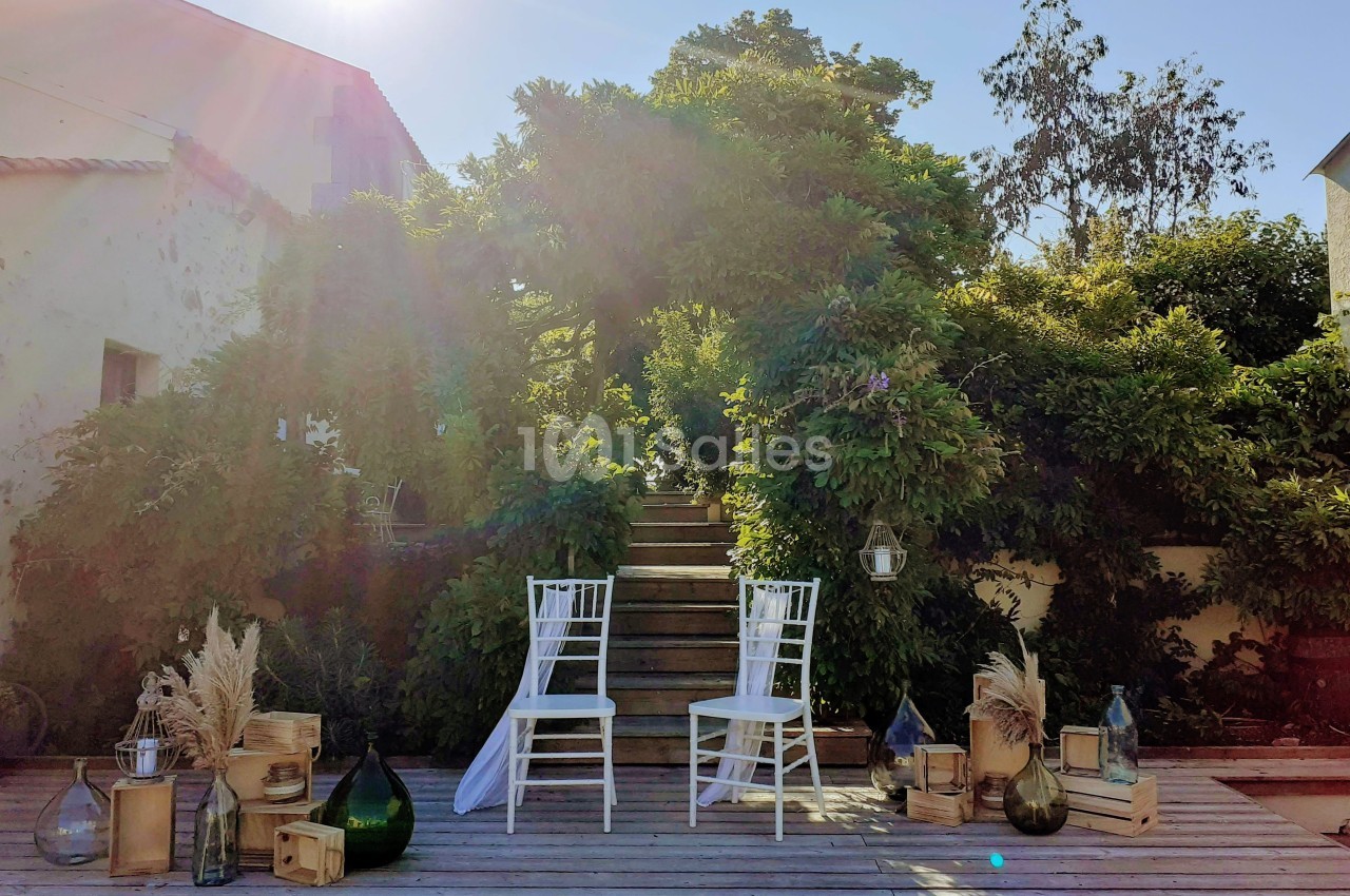 Deux chaises blanches disposées devant un escalier en bois entouré de verdure, avec des décorations naturelles.