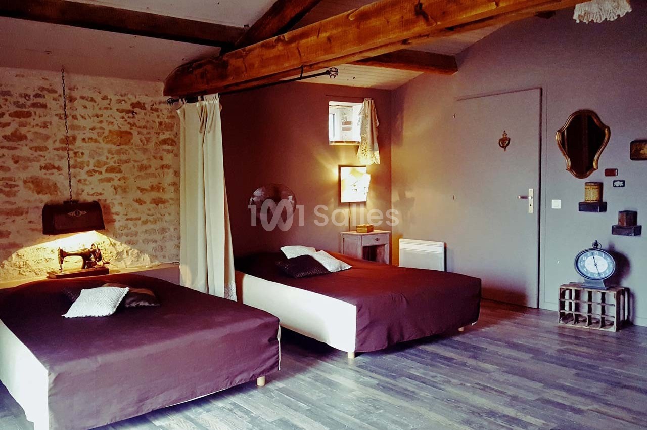 Chambre avec deux lits simples, murs en pierre et bois, éclairage chaleureux et décoration rustique.