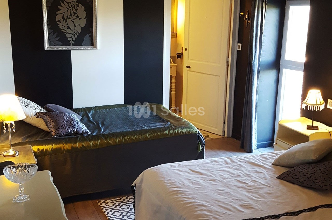 Chambre avec deux lits, décorée en noir et blanc, éclairée par une fenêtre et des lampes, avec une salle de bain attenante.
