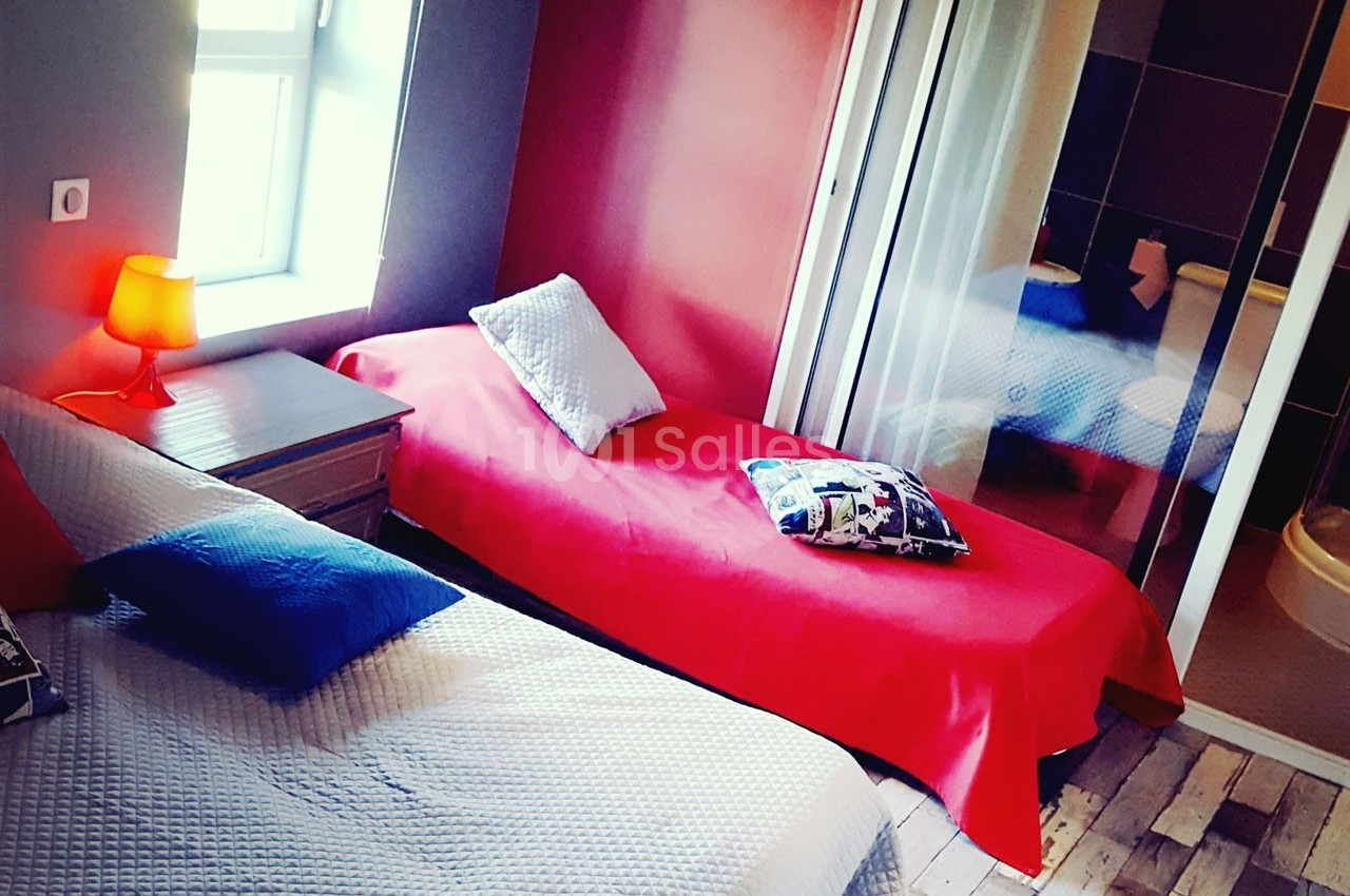 Chambre avec deux lits simples, linge coloré, lampe de chevet allumée et salle de bain attenante visible.