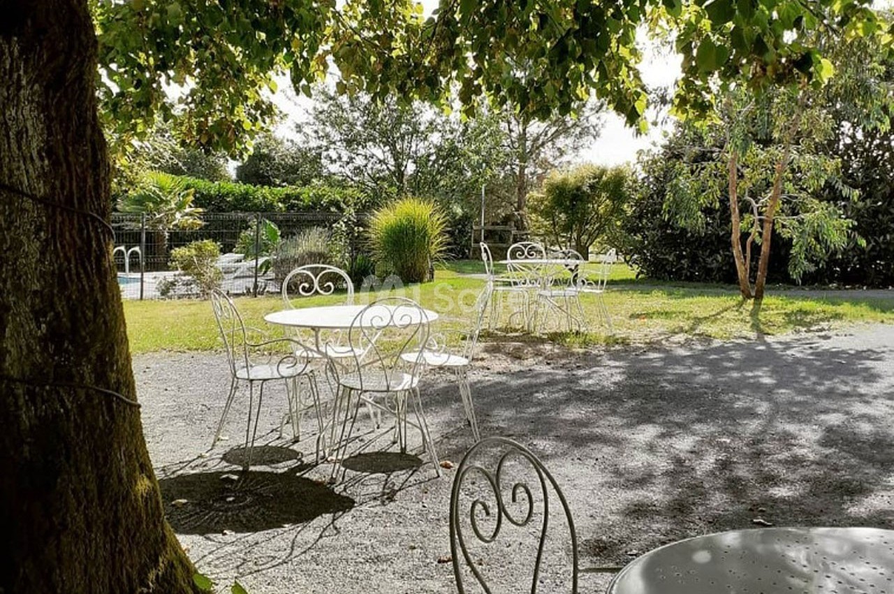 Chaises et tables blanches en fer forgé disposées sous des arbres dans un jardin ensoleillé.