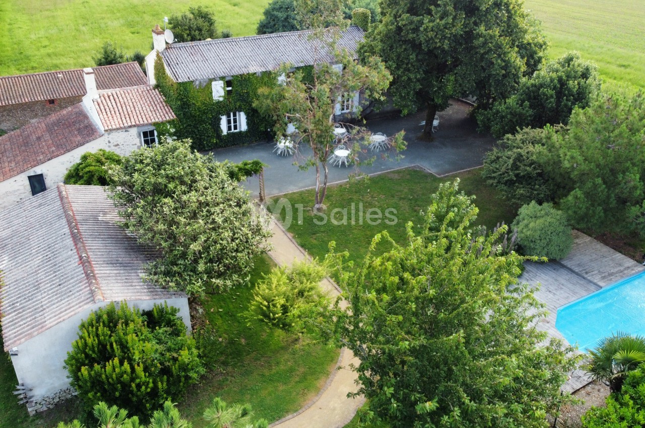 Vue aérienne d'une maison en pierre entourée de verdure, avec une piscine et une terrasse dans un jardin spacieux.