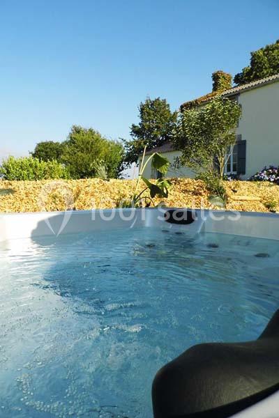 Vue d'un jacuzzi extérieur avec eau bouillonnante, entouré de végétation et d'une maison en arrière-plan.