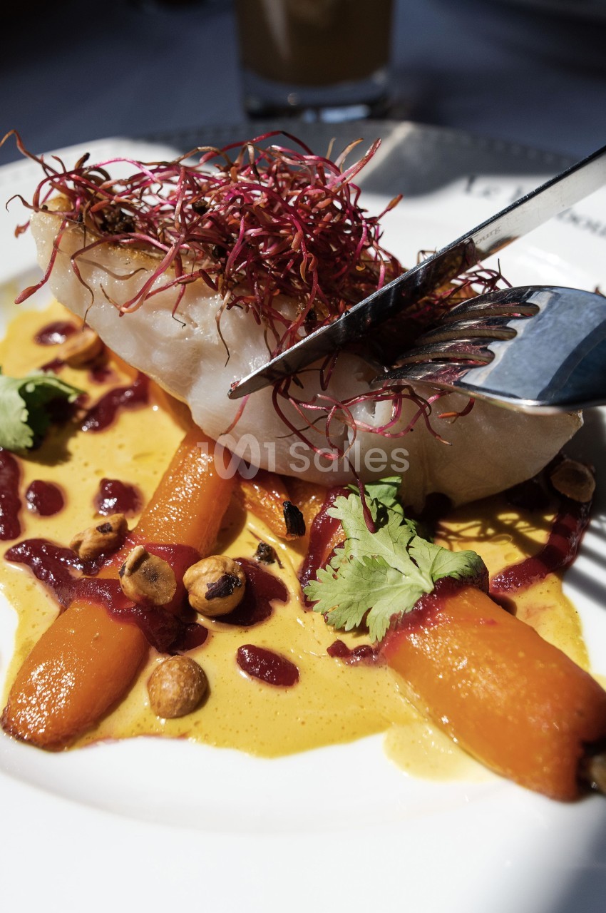 Filet de poisson avec carottes rôties, noisettes, sauce crémeuse et germes rouges, servi dans une assiette blanche.