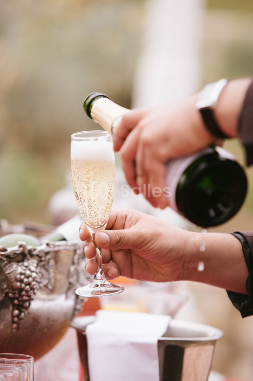 Une main verse du champagne dans une flûte tenue par une autre main, avec un seau à glace en arrière-plan.