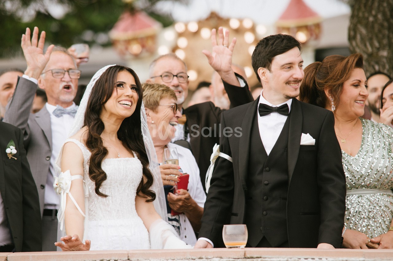 Un couple de mariés souriants entouré d'invités célébrant en plein air.