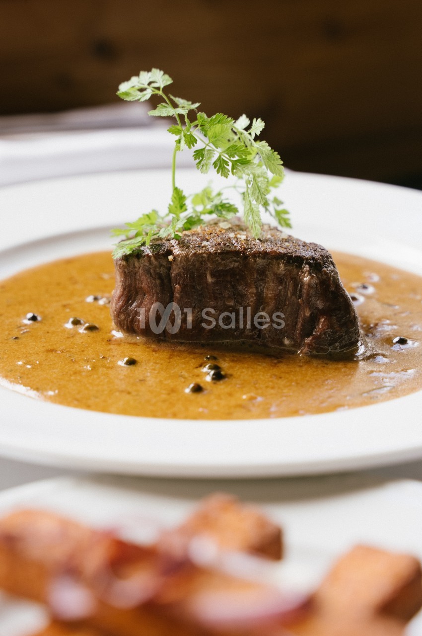 Pièce de viande servie avec une sauce au poivre, garnie de persil, présentée dans une assiette blanche.