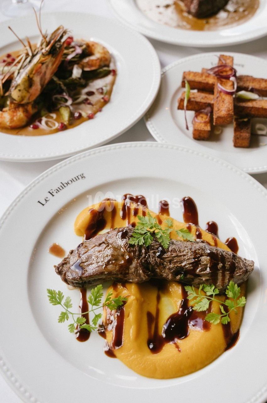 Assiette de viande grillée sur purée, nappée de sauce, accompagnée de crevettes et de frites de polenta.
