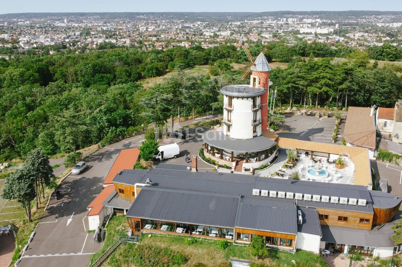 Vue aérienne d'un complexe avec un moulin rénové, une piscine et des bâtiments modernes entourés de verdure.