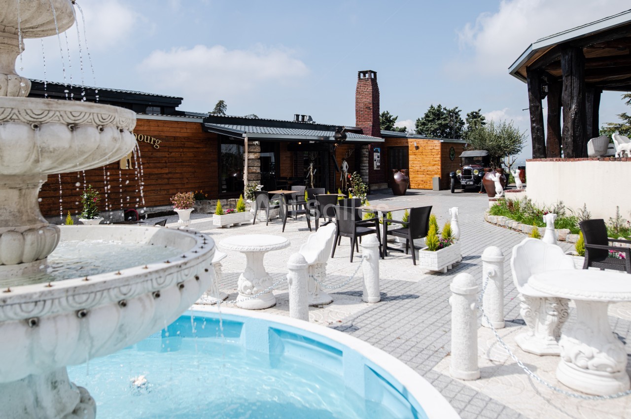 Cour extérieure avec une fontaine en premier plan, entourée de tables et chaises, devant un bâtiment en bois.
