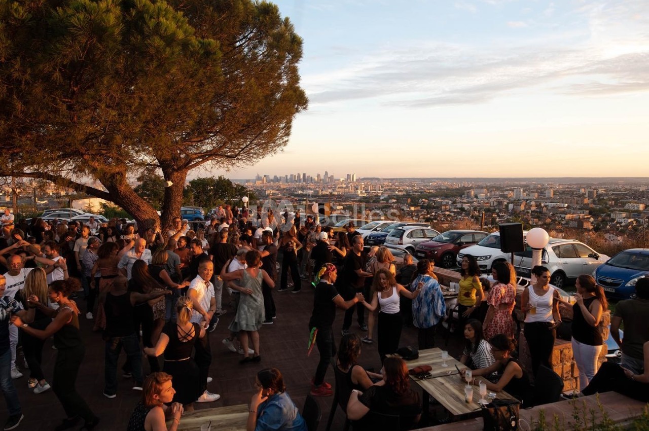 Groupe de personnes dansant et socialisant en extérieur au coucher du soleil, avec vue sur une ville en arrière-plan.