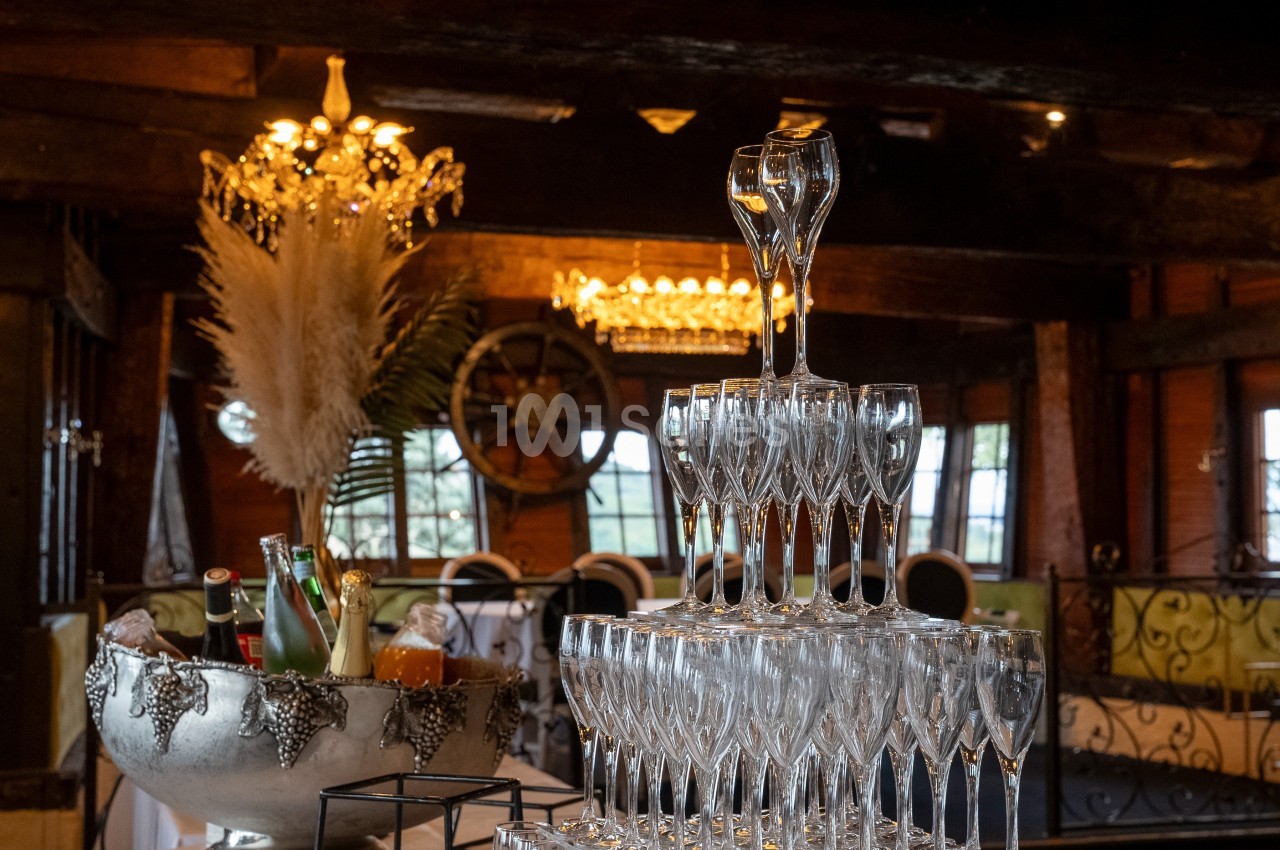 Pyramide de flûtes à champagne dans une salle décorée avec des chandeliers, des pampas et un seau à glace.