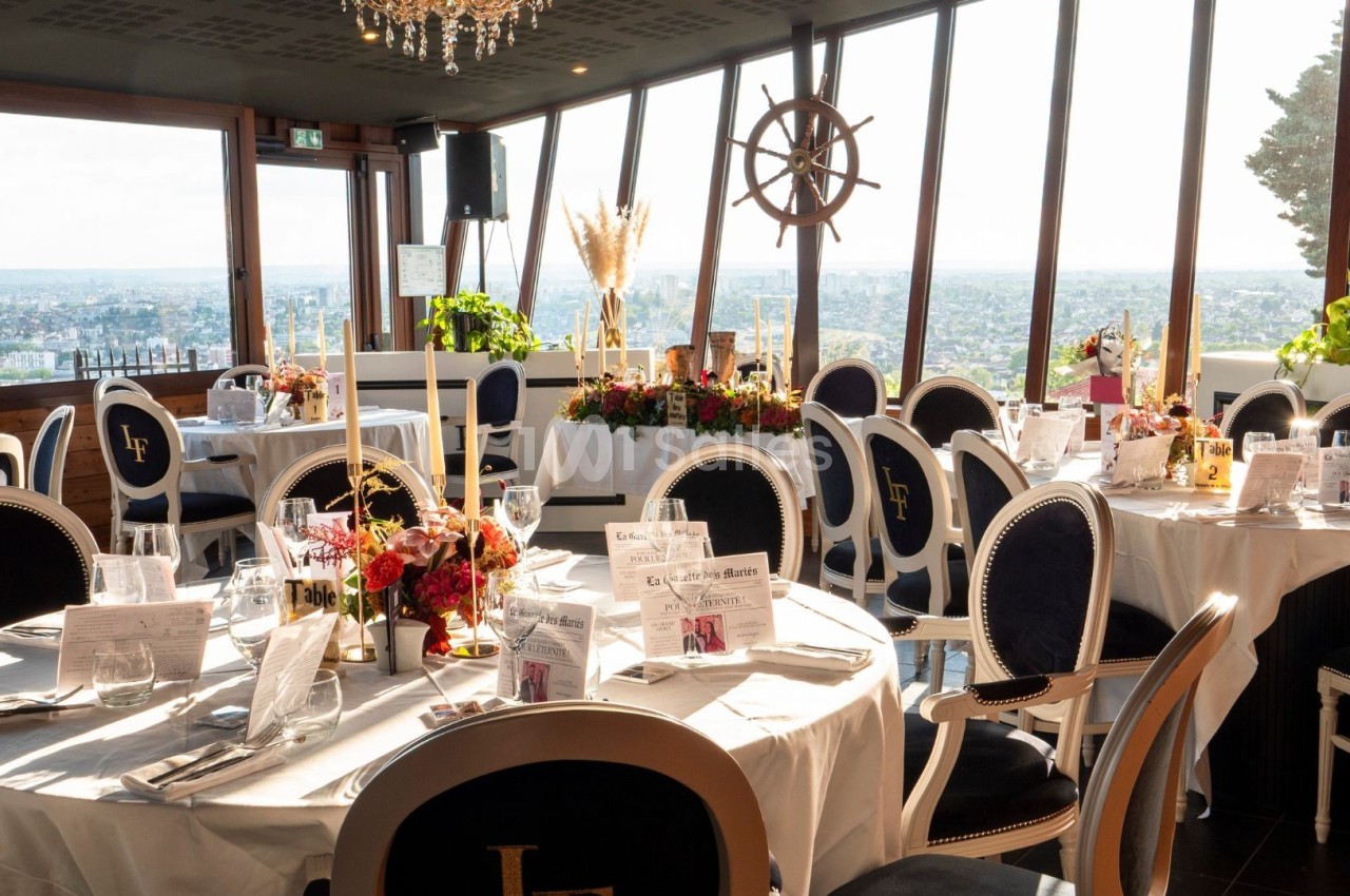 Salle de réception élégante avec tables rondes dressées, grandes baies vitrées offrant une vue panoramique sur la ville.