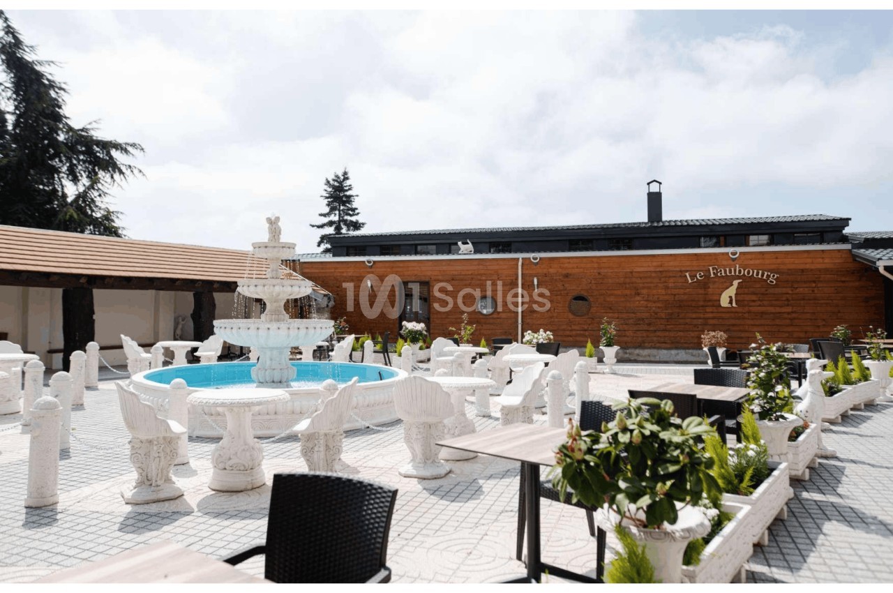 Cour extérieure avec une fontaine centrale, mobilier en pierre sculptée et bâtiment en bois en arrière-plan.