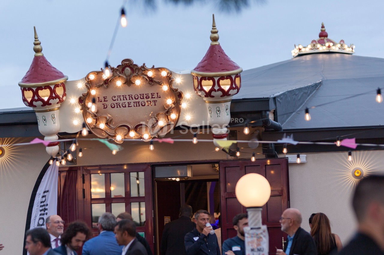 Entrée éclairée du Carrousel d'Orgemont avec des visiteurs rassemblés devant, sous des guirlandes lumineuses.