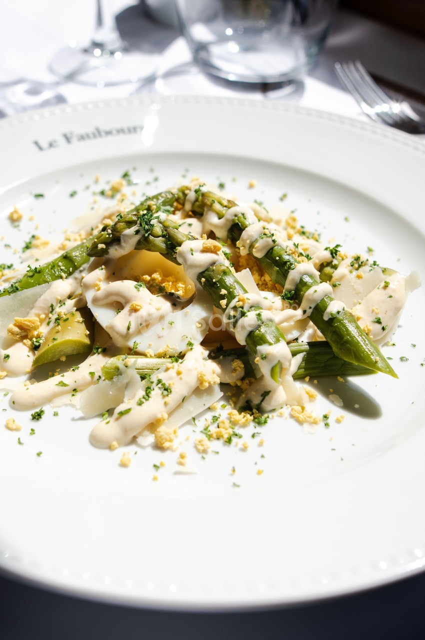 Assiette de légumes verts et blancs garnis de sauce crémeuse et d'herbes fraîches, servie sur une table lumineuse.