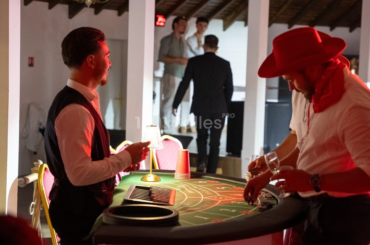 Un homme en costume anime une table de jeu de casino, tandis qu'un autre joueur mise des jetons.