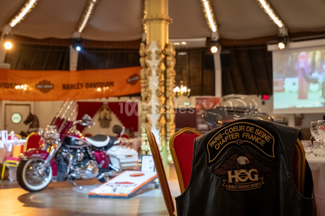 Salle décorée avec des éléments Harley-Davidson, une moto exposée et un gilet de motard posé sur une chaise.