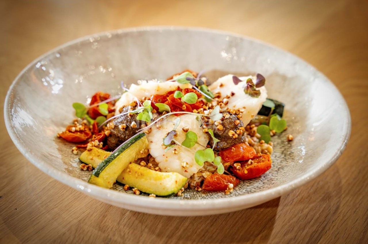 Assiette de légumes grillés avec courgettes, tomates cerises, herbes fraîches et céréales, présentée sur une table en bois.