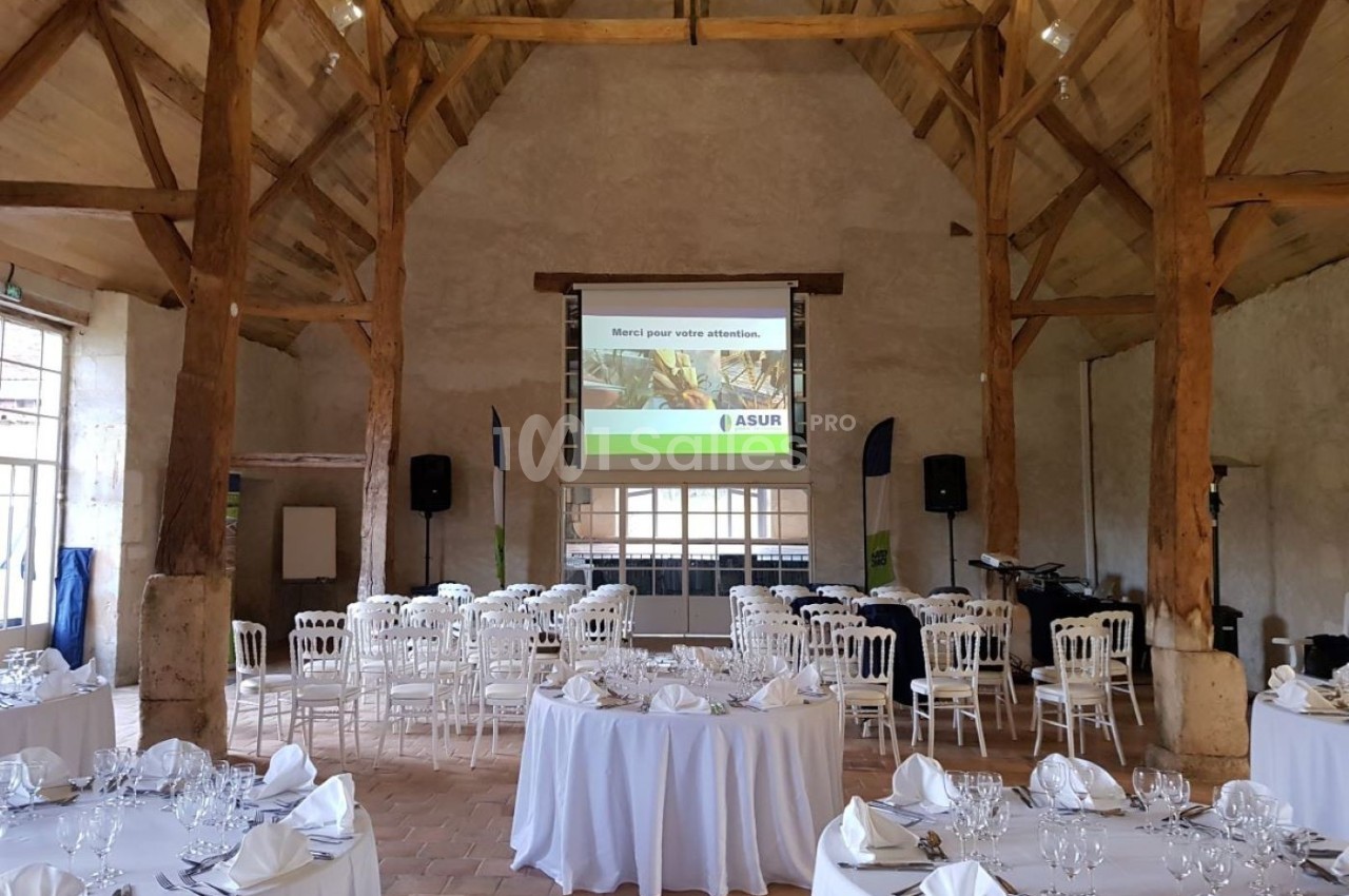 Salle de réception avec tables rondes dressées et écran de projection installé au fond de la pièce.