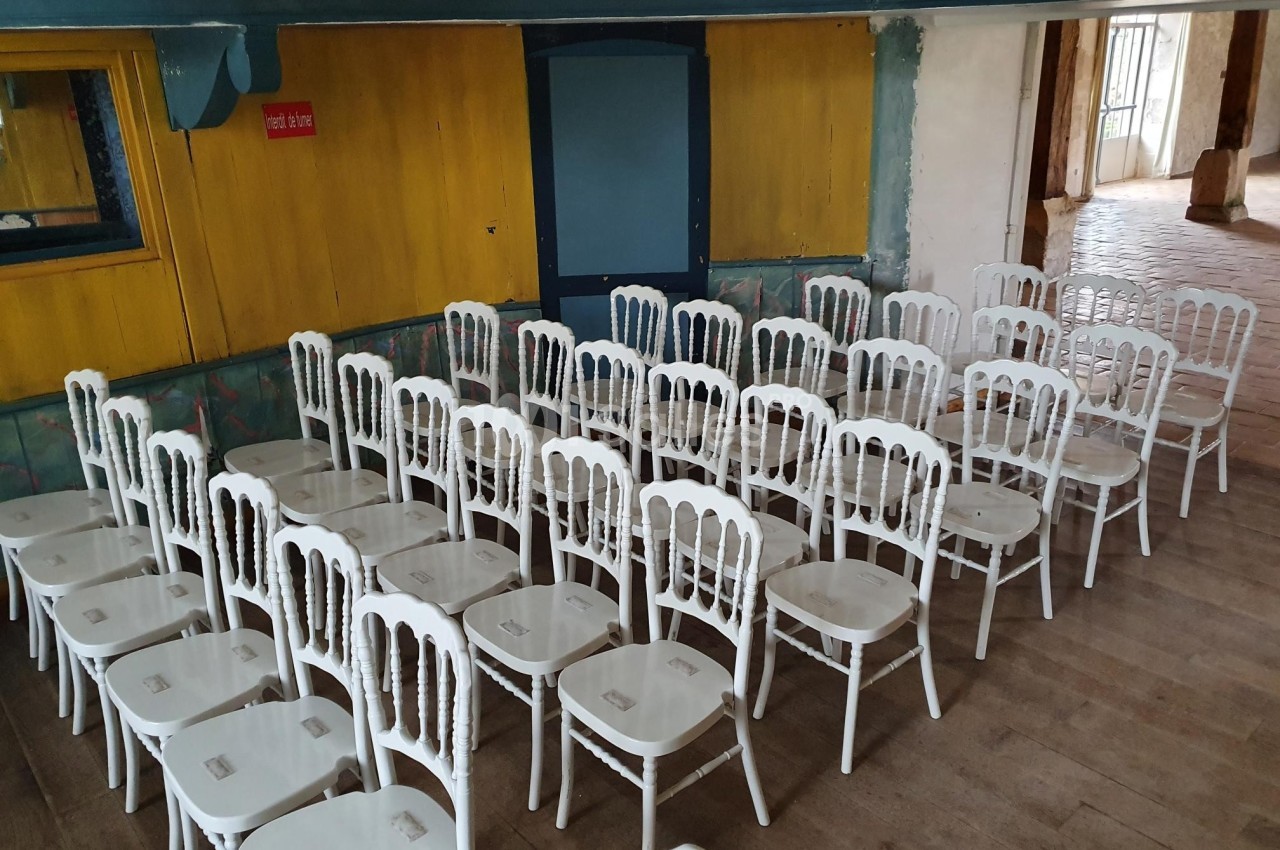 Rangées de chaises blanches alignées dans une salle aux murs jaunes et bleus, avec un sol en bois.