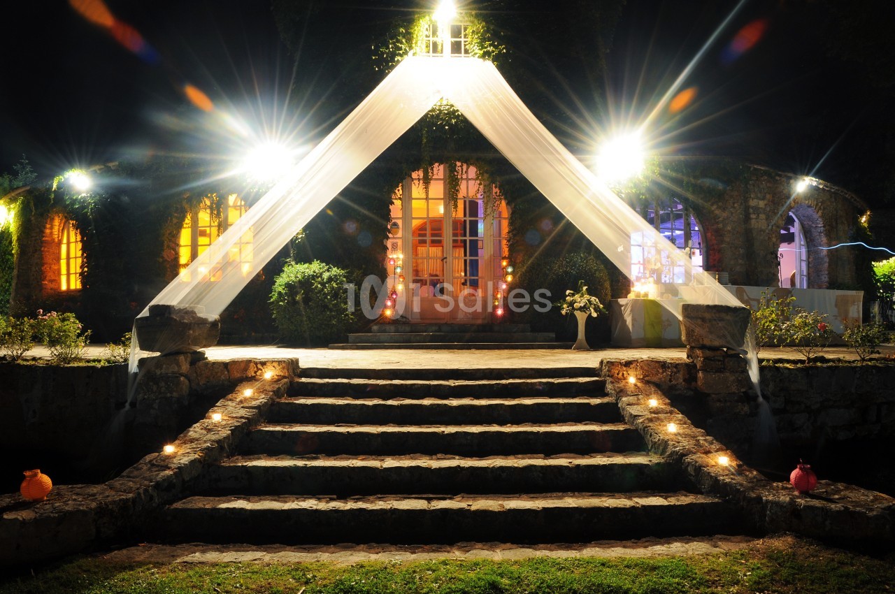 Entrée illuminée d'un bâtiment en pierre avec un escalier central, décorée de voiles et de lumières nocturnes.