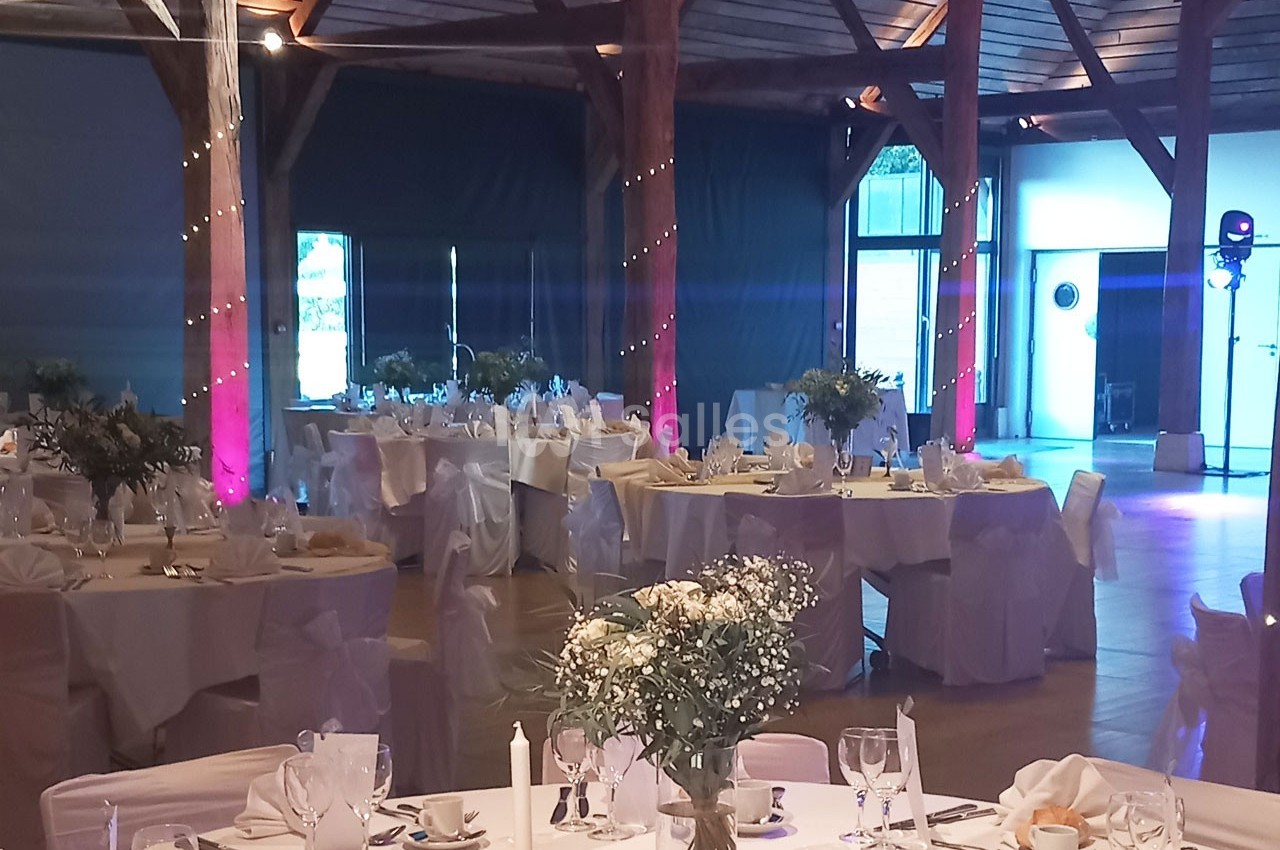 Salle de réception décorée pour un événement, avec tables dressées, nappes blanches et éclairage tamisé.