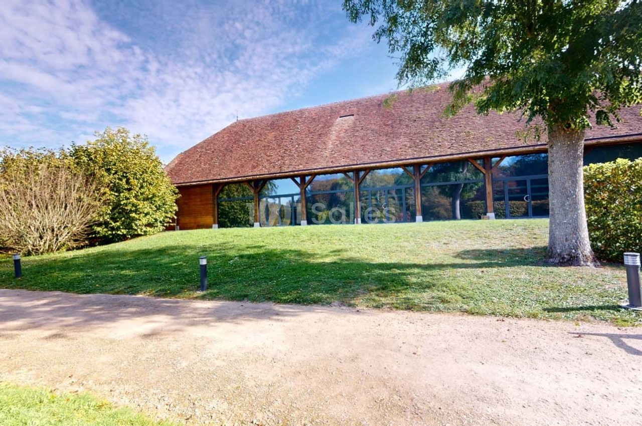 Bâtiment à toit en tuiles entouré de verdure, avec une façade vitrée et un chemin en premier plan.