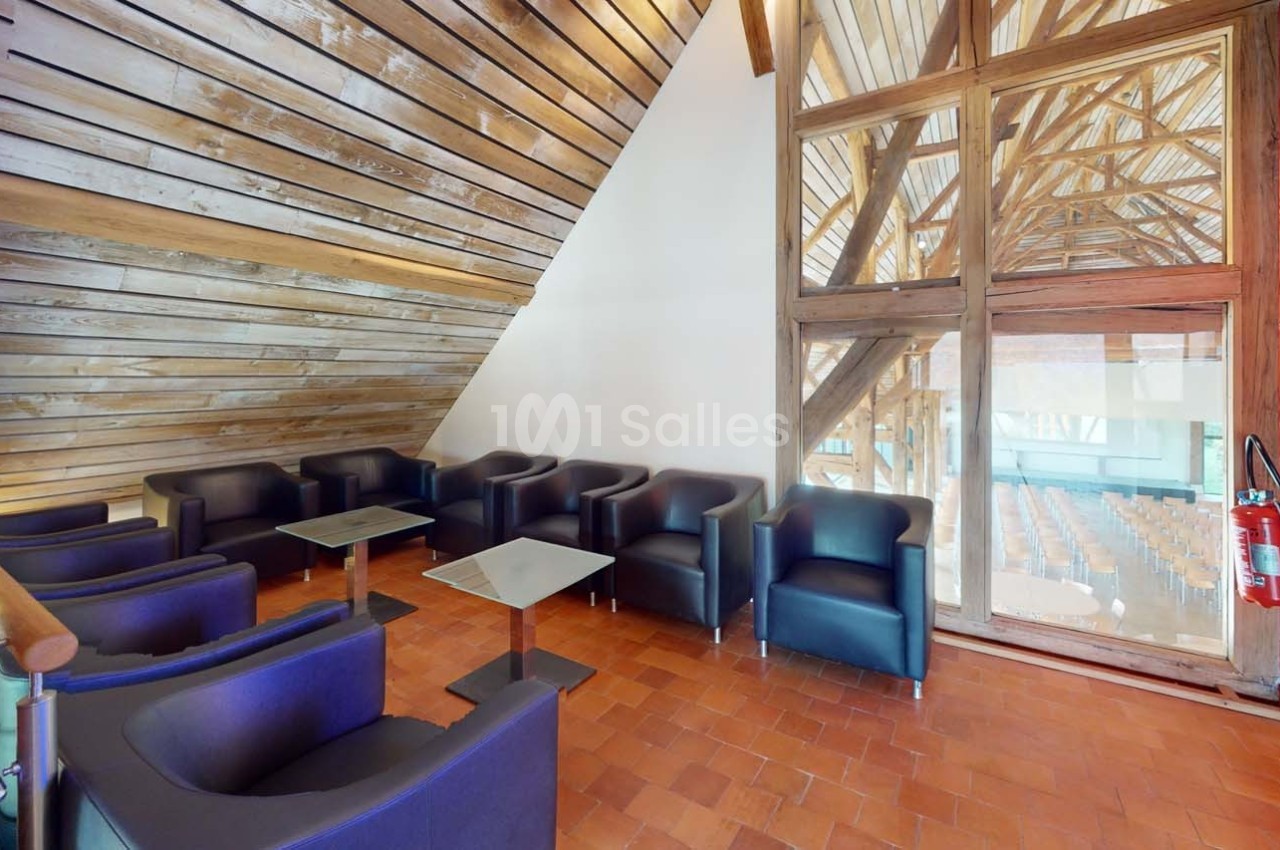 Salle avec des fauteuils noirs, tables basses, murs en bois et grande baie vitrée donnant sur une salle de conférence.