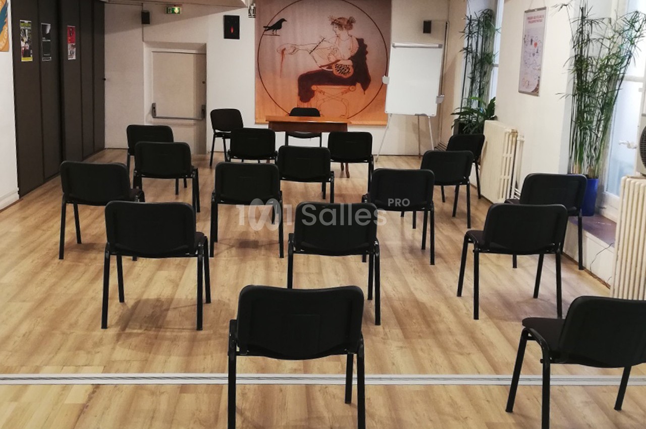 Salle de réunion avec des chaises noires disposées en rangées, tableau blanc et décoration murale en arrière-plan.