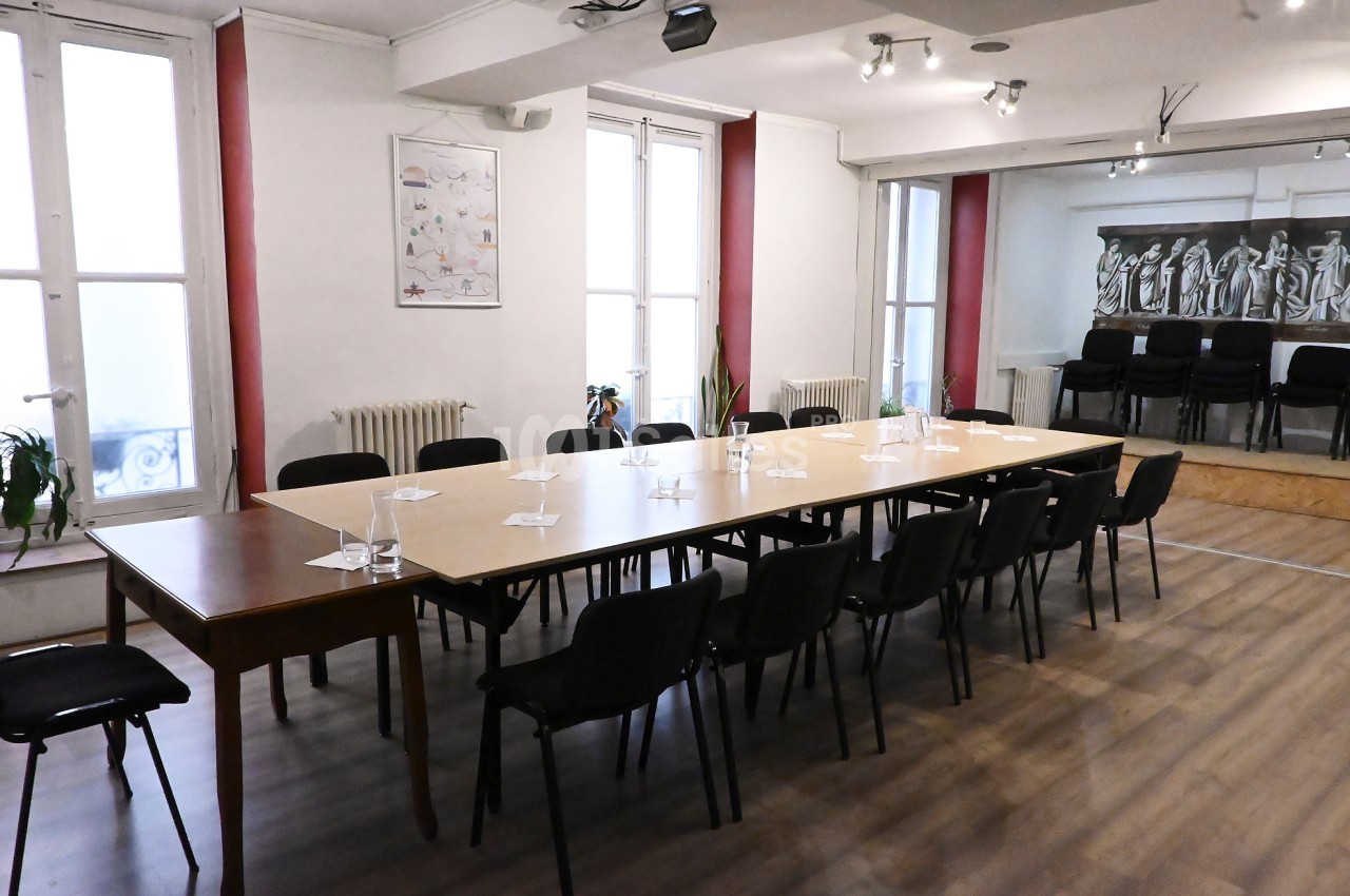 Salle de réunion lumineuse avec une grande table rectangulaire, des chaises noires et des fenêtres donnant sur l'extérieur.