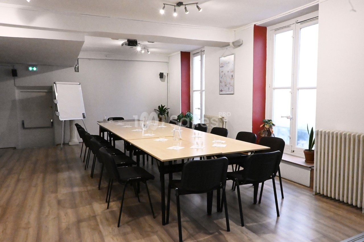 Salle de réunion lumineuse avec une grande table rectangulaire, des chaises noires et un paperboard.
