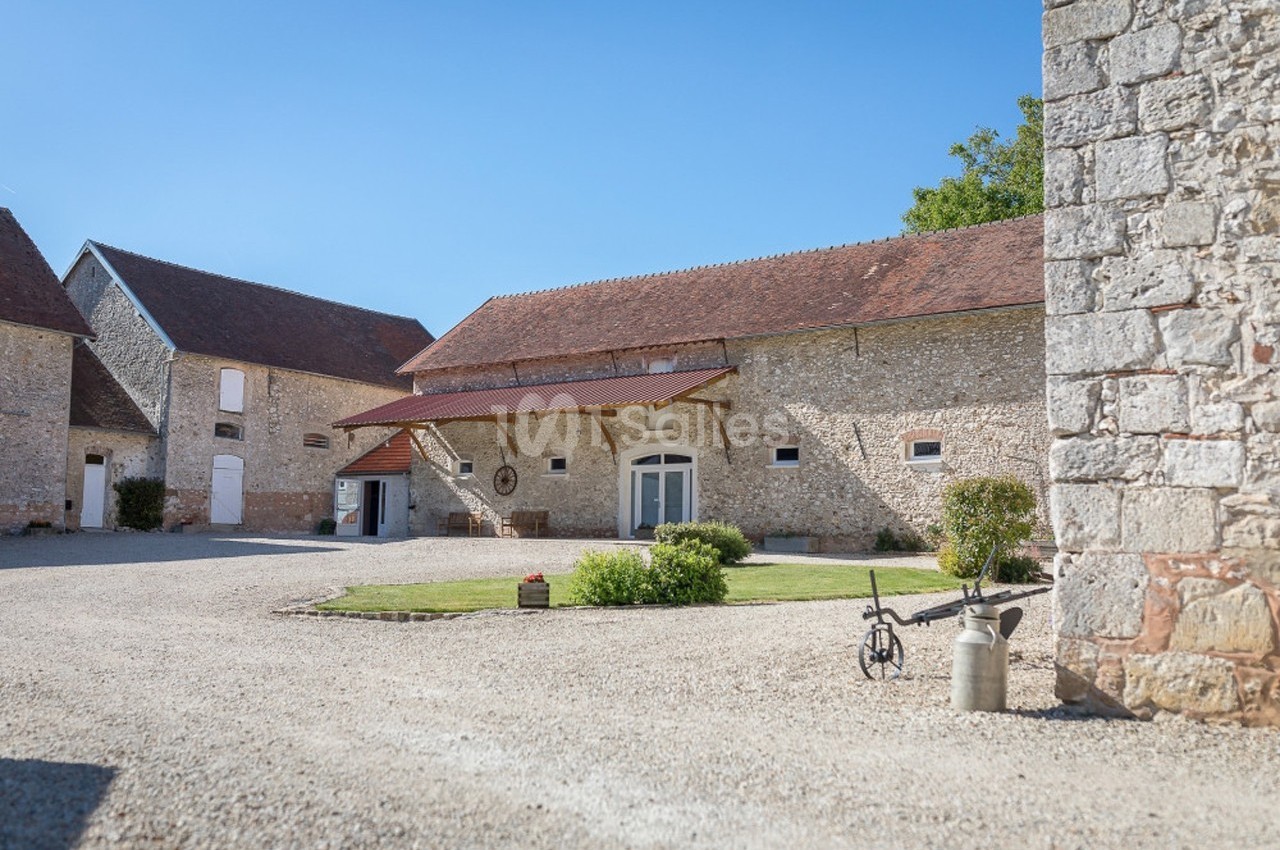 Cour d'une ferme en pierre avec bâtiments traditionnels, pelouse centrale et objets rustiques en décoration.