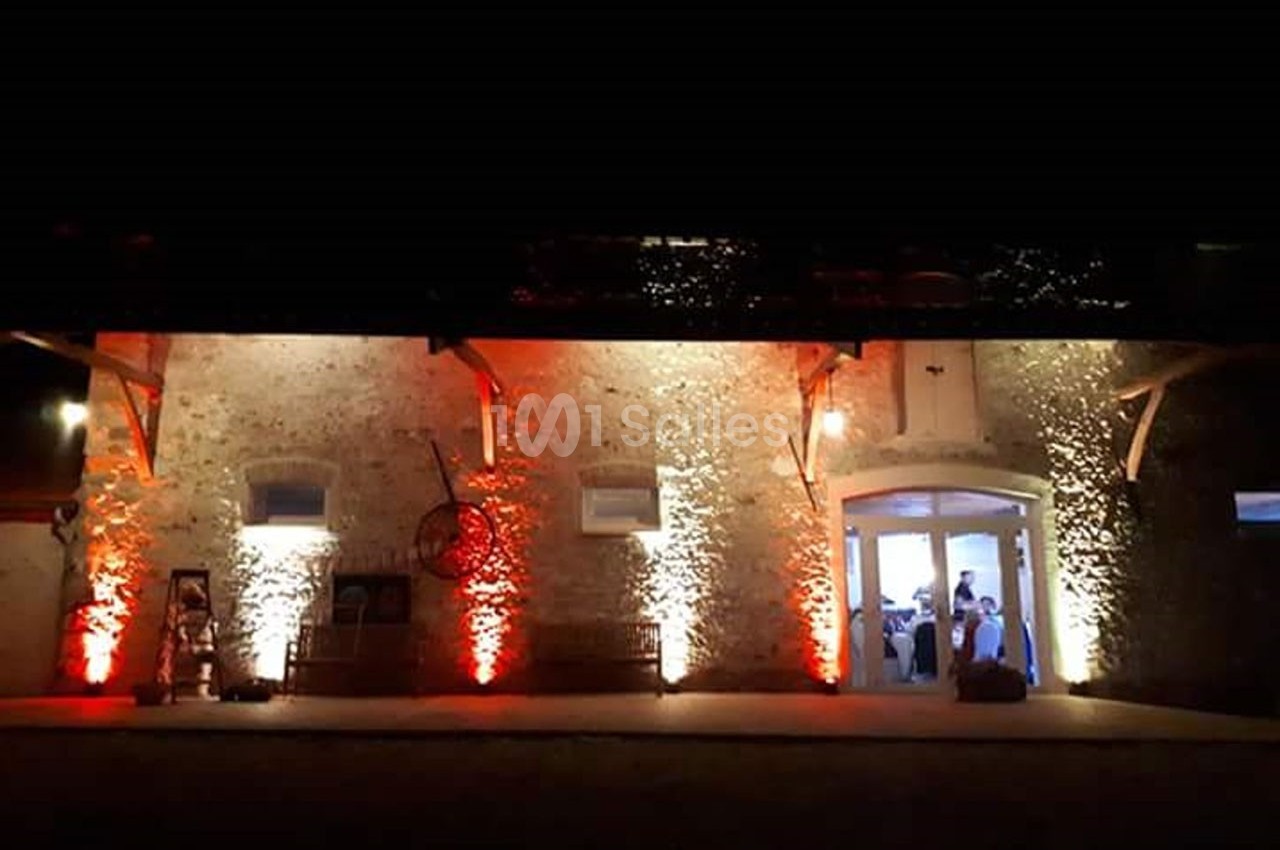 Façade en pierre éclairée par des lumières rouges et blanches, avec une porte ouverte laissant entrevoir un événement…