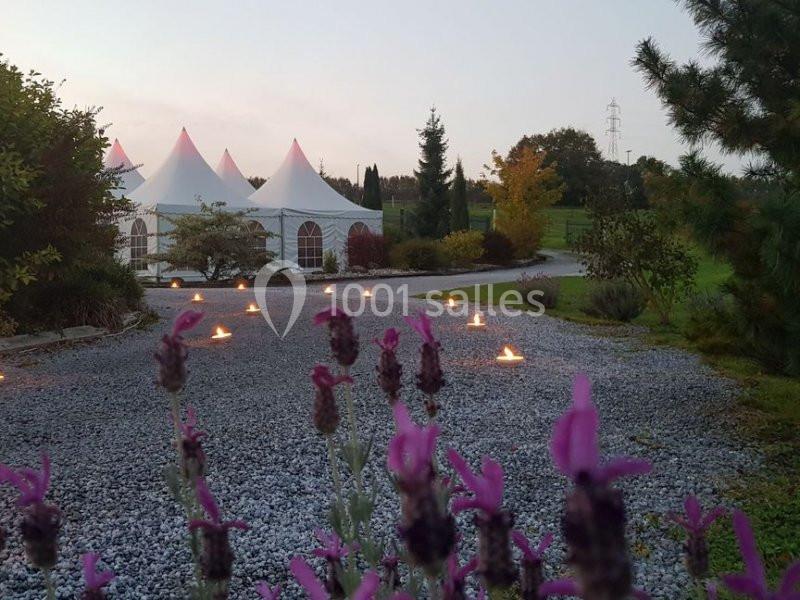 Allée en gravier bordée de lavandes et de bougies menant à des tentes blanches dans un jardin au crépuscule.