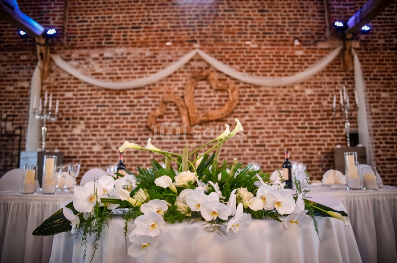 Décoration florale blanche sur une table de réception devant un mur en briques avec des ornements en bois.